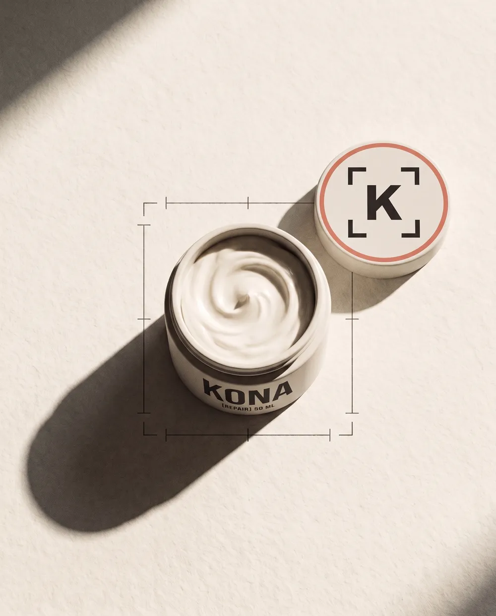 A cream jar with the Kona mark on its lid, under hard light on bone paper